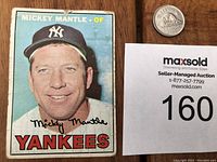 Front side of 1967 Topps Mickey Mantle baseball card showing player portrait with wearing Yankees cap. Coin for size and lot number card included.