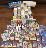 Wide view photo showing multiple stacks and boxes of baseball cards with various cards spread out in front, showcasing the volume and range of cards in the lot.