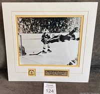 Matted black and white photo featuring Bobby Orr's famous goal and accompanying Boston Bruins pin with plaque.