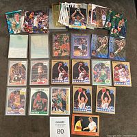 Photo showing an assortment of basketball cards including Larry Bird, Patrick Ewing, Latrell Sprewell, Charles Barkley, Magic Johnson, Shawn Kemp, and others, laid out on a dark surface.