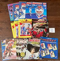 Photo showing the 15 hockey sticker albums laid out on wooden floor. Varied cover designs including O-Pee-Chee and Panini brands, multiple years from early 1980s to mid-1990s.
