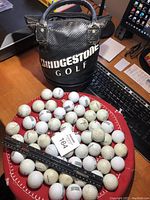 Photo of over 60 golf balls on a red surface alongside a Bridgestone Golf branded black carrying case.