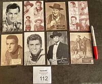 Lot of 8 vintage Western stars exhibit cards laid out on dark brown surface with a red marker showing scale. Cards have black & white and sepia tones.