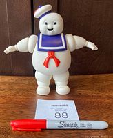 Frontal view of the Stay Puft Marshmallow Man figurine standing on a wooden surface with a red Sharpie placed in front for size comparison.