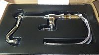 Chrome faucet set inside protective black foam insert within the box, showing the faucet assembly and attached hoses.