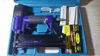 Central Pneumatic air brad nailer stapler tool in blue plastic carrying case with trigger, air hose connector, and black magazine for nails/staples. Includes two boxes of staples.