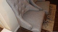 Side view of one gray upholstered chair showing tufted details and wooden legs.