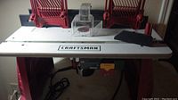 Front view of entire router table showing white top, red base, Craftsman logo, fences and clear guard
