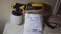 Wagner Flexio 570 paint sprayer sitting on white surface with owner's manual and power cord visible.