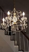 Crystal chandelier lit with 5 candelabra style bulbs, featuring drops and beads of clear crystal and gold tone metal framework.