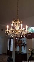 Full view of the crystal chandelier hanging in a room with 7 light bulbs lit, showing its size and setting.