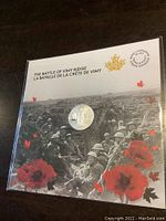 Front view of the sealed commemorative coin with background image of soldiers and red poppies.