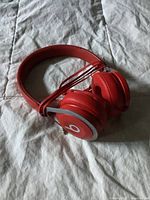 Red Beats wired headphones laid on a gray textured fabric surface showing overall design and cable coiled around one ear cup.