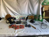 Photo showing entire lot including vintage rotary phone, desk light, calculator, art supplies, batteries, small hammer, decorative bead artwork, and additional small items.