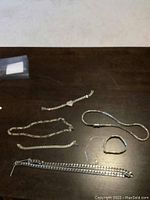 A collection of various silver-colored jewelry pieces including bracelets, necklaces, and chains arranged on a dark wooden surface.