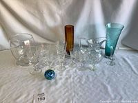Overview of all lot items including glassware, pitcher, vases, and glass paperweight on white cloth