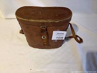 Leather carrying case for binoculars, showing brown worn exterior with buckle closure and strap.