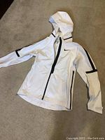 White Nike Aerosheild jacket laid out showing front with hood, full zip, black accents on sleeves and pocket seams