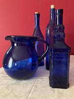 All four blue glass items together showing one large round water jug and three tall narrow corked bottles, one with square faceted shape