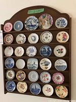 Overall display of thirty miniature decorative plates on a brown wooden display rack sized 19x24 inches highlighting the variety in colors and designs