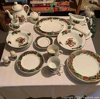 Full set of Christmas dinnerware arranged on table showing plates, bowls, cups, saucers, serving pieces.