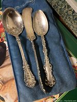 Three ornate silverplate serving pieces on blue cloth