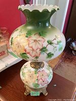 Full front view of electric hurricane lamp showing the hand-painted glass globe with flowers and the ornate metal base on a wooden table.