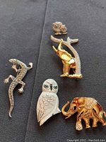 Five animal brooches (lizard, owl, two elephants, sheep) on black cloth