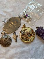 Photo showing large fish-shaped pendant, shell pendant, cross pendant, round painted pendant, angel charm in plastic bag, and amethyst cluster pendant on fabric background.