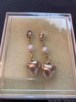 Close-up of a pair of gold-tone dangle earrings with chain, pearl bead, and heart pendant showing details of design and material