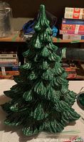 Large green ceramic Christmas tree shown standing upright on a table with textured leafy branches layered throughout the tree.