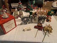 Overview of all items on plaid cloth including mosaic candles, bowl, ceramic Christmas trees, signs, figures and gold reindeer.