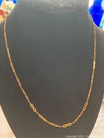 Gold toned chain necklace displayed on black stand showing unique geometric rectangular links.