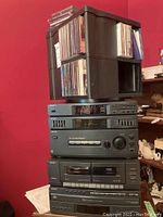 Stacked Sony stereo components including equalizer, tuner, cassette player, CD changer with plastic crate holding CDs on top.