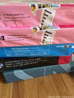 Stack of HP and Xerox multipurpose printer paper reams in pink and blue packaging.