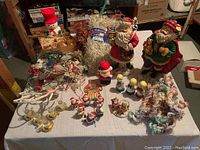 Wide view of collection on table including Santa figurines, choir girls, snowman, string lights, candle holders, and tinsel garlands