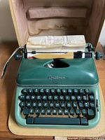Front view of the sage green Optima Super typewriter with keys visible and some old paper loaded.