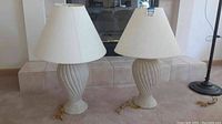 Two matching stone or terra cotta style table lamps with twisted spiral bases and beige fabric shades, placed side by side.