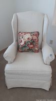 Front view of cream/ivory striped wingback side chair with floral decorative pillow on the seat.