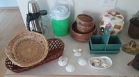 Photo showing assorted kitchen and decor items including baskets, bowls, thermos, cooler, cookie jar, shells.