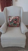 Front view of cream/ivory striped wingback chair with floral decorative pillow on seat.