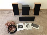 All four Klipsch home theater speakers positioned on the floor with some Monster Cable speaker wires and Klipsch manuals visible in front of them.