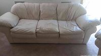 Full view of cream colored leather sofa with three cushions, minor wear visible on cushions.