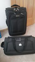 Front view of Delsey black rolling suitcase and black duffle bag