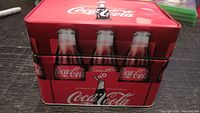 Front view of red Coca-Cola tin recipe box showing three classic Coca-Cola bottles and the brand logo.