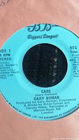 Label of Side 1 of the 45 RPM vinyl record showing song "Cars" by Gary Numan on Beggars Banquet label with blue background.