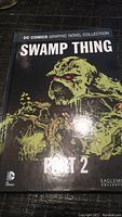 Front cover of Swamp Thing Part 2 graphic novel showing main character with green and black illustration and red eyes.