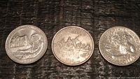 Three U.S. quarters laid out in a row showing their reverse designs: Harriet Tubman statue and childhood home, Iwo Jima Memorial, Abraham Lincoln log cabin.