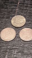 Three round brass tokens with different embossed designs placed on dark textured surface.
