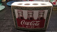Front view of vintage Coca-Cola ceramic toothbrush holder showing three classic Coke bottles and Coca-Cola logo with price text.
